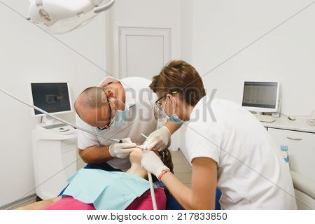 Process of preparing and installing dental ceramic crown. Male professional dentist and female assistant helps to treat the teeth of woman patient in clinic light office with modern tools equipment