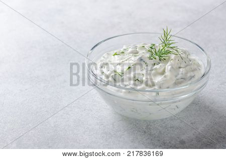 Homemade greek tzatziki sauce in a glass bowl on a light stone background. Close-up, horizontal image, copy space