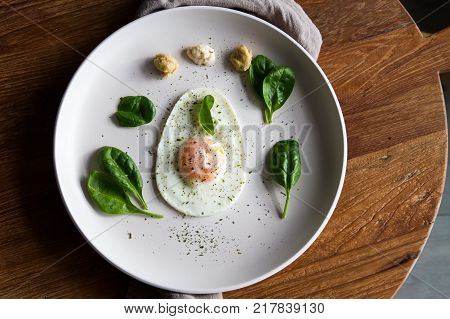 Single Fried Egg In Egg Shape Over White Plate Garnished With Spinach Green Herbs Salt Papper Horser