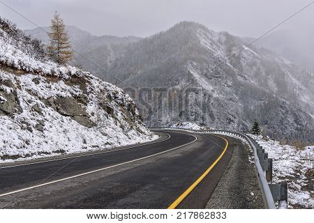 Scenic view of the hairpin bend winding road through the pass part of a mountain serpentine in the autumn cloudy weather with snow