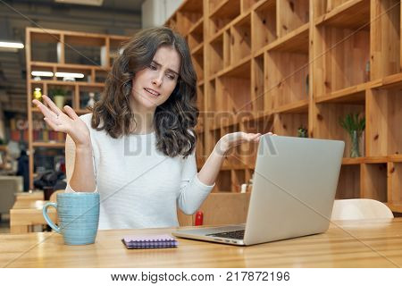 a young girl with long curly hair sitting in a cafe with a laptop throws her arms out to the side with uncomprehending unhappy upset expression