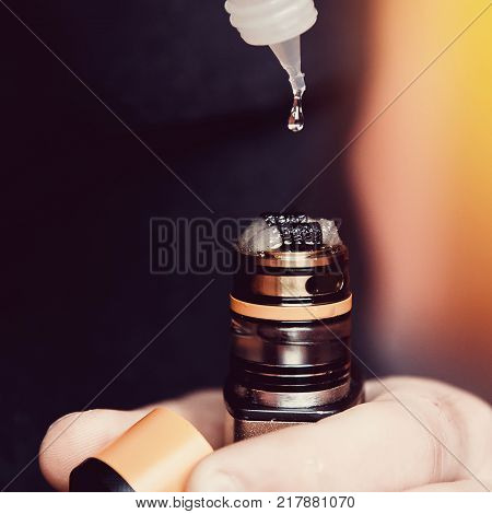 Close-up of man dripping fragrant liquid on cotton wool electronic cigarette. Nichrome heated. The concept of safe replacement of cigarettes and tobacco.