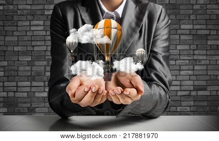 Closeup of business woman in suit presenting flying aerostate among clouds in her palms with dark brick wall on background. 3D rendering.