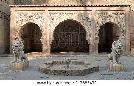 Cairo, Egypt - December 2, 2017: Two white marble lions statues and decorative fountain in front of three adjacent decorated stone arches at the garden of Manial Palace of Prince Mohammed Ali located in Manial district