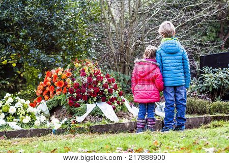 Little brother and sister standing at the grave of their parents in the graveyard