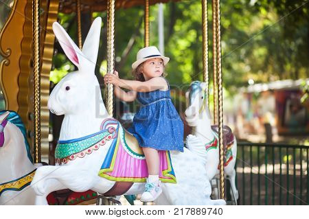 Cute little girl at the theme park riding retro merry-go-round carousel.
