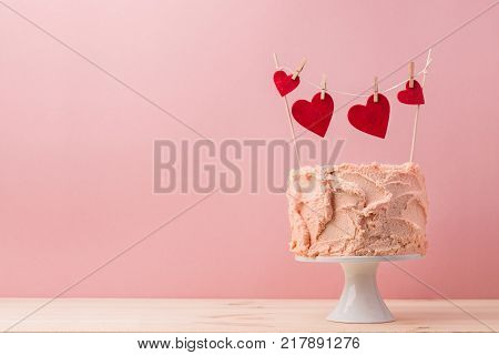 Pink sweet cake with decorative red hearts garland on top composed on pink.