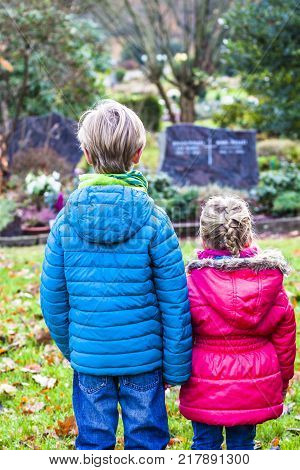 Little brother and sister standing at the grave of their parents in the graveyard
