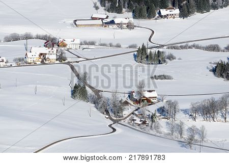 Idyllic rural countryside on snowy winter day. Aerial view of barnyards and farms. Weitnau, Allgau, Bavaria, Germany. Typical bavarian cultured landscape.
