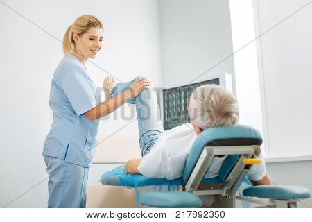 Professional medicine. Cheerful delighted skillful woman holding her patients leg and smiling while enjoying her job