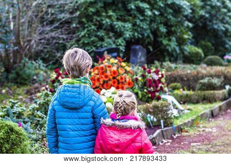 Little brother and sister standing at the grave of their parents in the graveyard