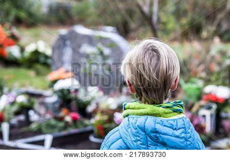 Little boy standing at the grave of his parents in the graveyard