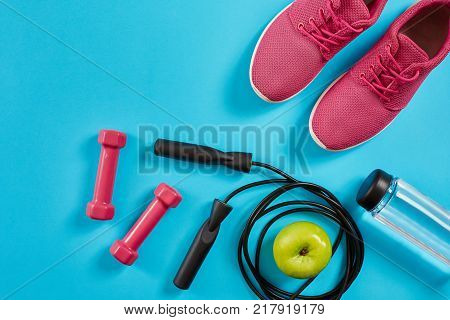 Flat lay of female sport equipments, jump rope, bottle of water and pink sneakers on blue background. Sports and healthy lifestyle concept. Top view. Copy space. Still life