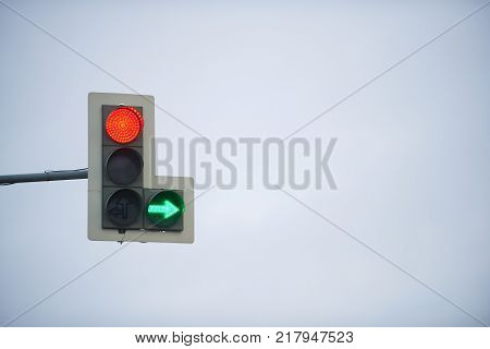 Traffic light with stop signal and green arrow on the background of cloudy sky