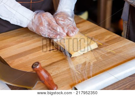 Packing order at grocery shop in cling film on wooden table, background. Shop assistant wrapping a piece of cheese.