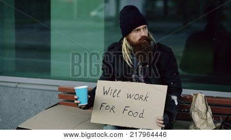 Homeless young man beg for money shaking cup to pay attention people walking near beggar at city street