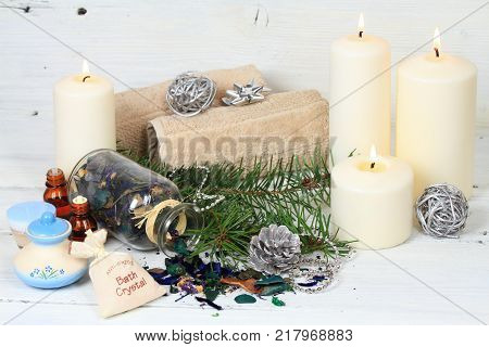 Winter spa concept with candles. Wellness objects aromatic herbs anti stress bath crystals essential oil and body cream on white wood table.