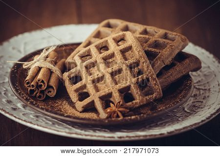 Closeup of Chocolate Viennese Belgian homemade waffles and cinnamon sticks on a large plate. Homemade pastries. A vintage effect. Tinted