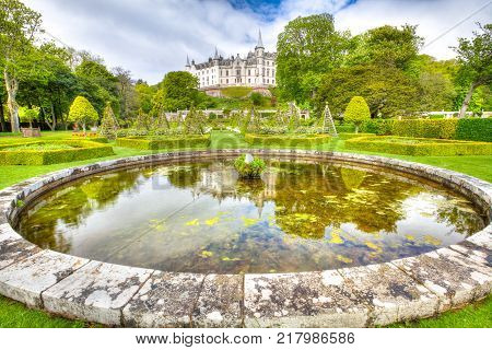 Dunrobin Castle reflected on the pond inside a beautiful and spectacular park that surrounds it. Dunrobin gardens have beautiful fountains, and labyrinth hedges. Scottish Highlands, Scotland, UK.