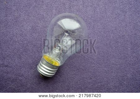 A round ordinary non-economical incandescent bulb with a transparent socle background of purple cloth.
