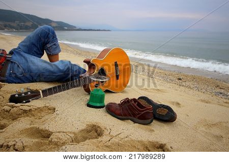 Man sitting on the beach with guitar and shoes. Travel conception.