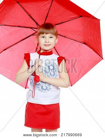 A nice little blonde girl with a short bangs. In a red skirt and a white T-shirt with a pattern. The girl hid under the red umbrella.