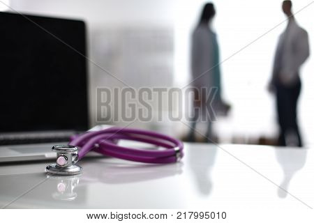 Laptop and medical stethoscope on the desk , doctors standing in the background.