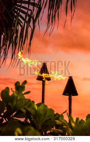 Hawaii luau party Maui fire tiki torches with flames burning against sunset sky clouds at night. Hawaiian culture travel background.