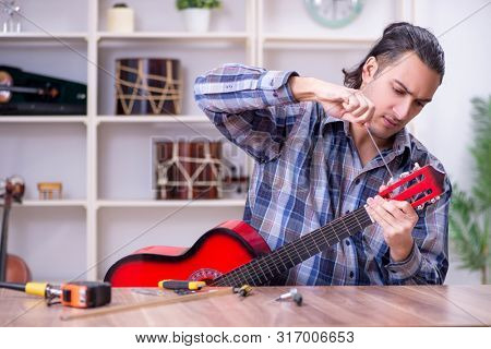 Young handsome repairman repairing guitar