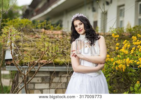 Smiling Sexy Caucasian Bride With Diadem Posing In Flowers Garden Outdoors. Wearing Beads Necklace. 