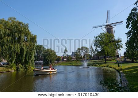 Leiden, Holland - July 26, 2019: Sailing a recreational boat with the historical tower mill de Valk, the Falcon, in the background 