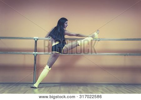 Beautiful Young Dancer Demonstrating Her Flexibility Standing Near Ballet Barre At Empty Dance Hall 