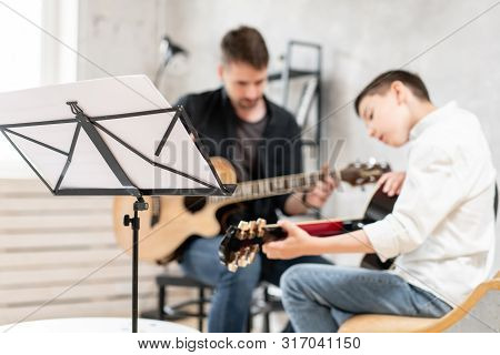Young Teenager And His Older Brother Learining To Play Acoustic Guitar Together