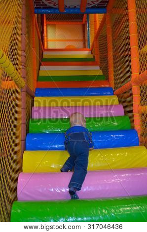 A Boy In Denim Overalls Climbs Up The Multi-colored Stairs