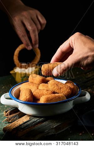 closeup of a man picking a spanish croquette from a white and blue enamel plate, and another man dipping a calamar a la romana, a fried battered squid ring typical of spain, in aioli sauce