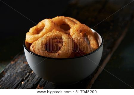 closeup of a white ceramic bowl with calamares a la romana, fried battered squid rings typical of spain, on a dark rustic wooden table