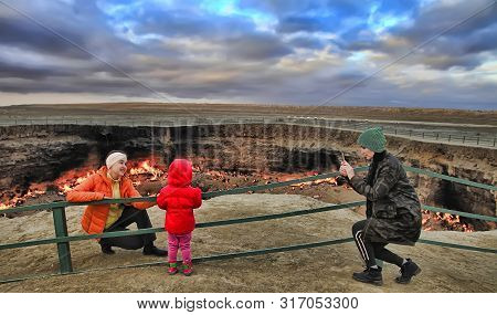 Turkmenistan, Darvaza - March 21, 2019: Girls Make A Photo On The Background Of The Burning Crater 
