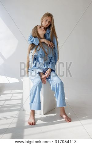 Two Young Beautiful Twin Sisters Posing In Blue Suits On White Studio Cyclorama In Pattern Of Light 