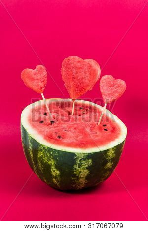 Half Ripe Juicy Watermelon Decorated With Decorative Hearts On A Wooden Stick Isolated On A Red Back