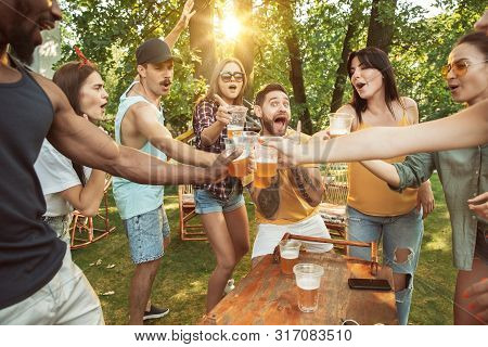 Group Of Happy Friends Having Beer And Barbecue Party At Sunny Day. Resting Together Outdoor In A Fo