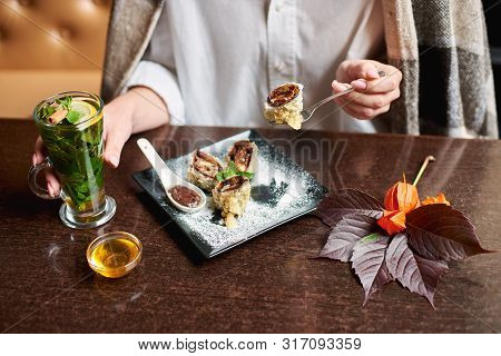 Crop Of Woman In White Holding Drink In Hand And Eating Tasty Sweet Sushi Roll With Chocolate Sauce.