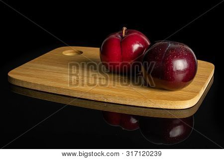 Group Of Two Whole Ripe Red Round Plum On Bamboo Cutting Board Isolated On Black Glass