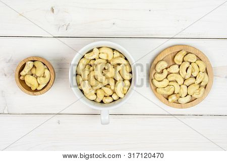 Lot Of Whole Unsalted Beige Cashew On Round Bamboo Coaster In Tiny Wooden Bowl Flatlay On White Wood