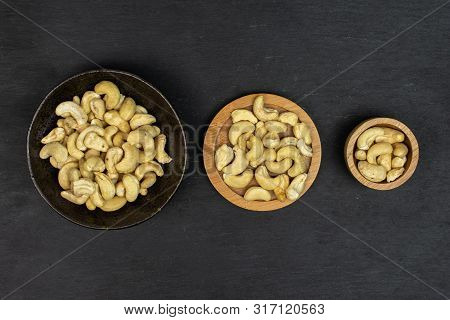 Lot Of Whole Unsalted Beige Cashew On Round Bamboo Coaster In Tiny Wooden Bowl In Dark Ceramic Bowl 
