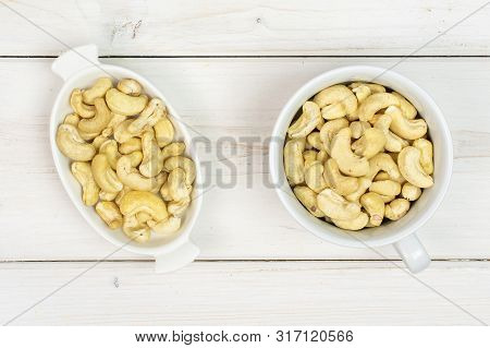 Lot Of Whole Unsalted Beige Cashew In White Oval Ceramic Bowl Flatlay On White Wood