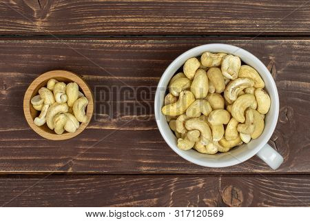 Lot Of Whole Unsalted Beige Cashew In Tiny Wooden Bowl Flatlay On Brown Wood