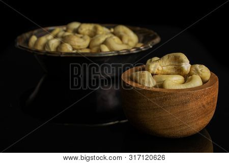 Lot Of Whole Unsalted Beige Cashew In Tiny Wooden Bowl In Metal Bowl Isolated On Black Glass