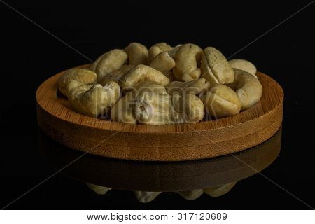 Lot Of Whole Unsalted Beige Cashew On Round Bamboo Coaster Isolated On Black Glass