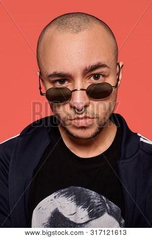 Studio Shot Of A Young Tattoed Bald Man Posing Against A Pink Background. 90s Style.
