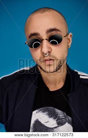 Studio Shot Of A Young Tattoed Bald Man Posing Against A Blue Background. 90s Style.
